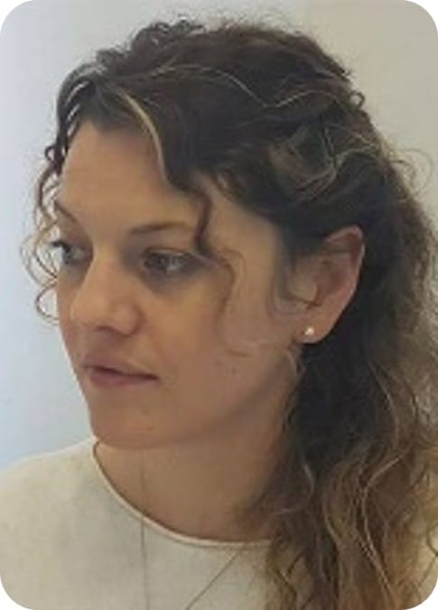 A woman with wavy brown hair pulled back looks to the left. She is wearing a light-coloured top and small stud earring, her neutral expression reflecting quiet focus—perhaps contemplating her work in MultiStress Research or food security.