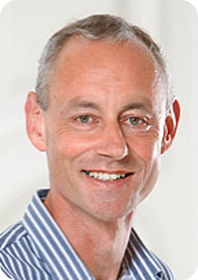 A middle-aged man with short grey hair, wearing a blue and white striped shirt, smiles at the camera against a plain light background—passionate about crop modelling and its role in advancing food security.