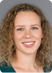 Portrait of a woman with curly light brown hair, fair skin, and green eyes, smiling at the camera against a plain grey background—ideal for MultiStress Research or Crop Modelling projects focused on advancing food security.