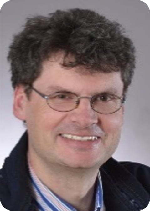 A man with curly brown hair and glasses smiles at the camera, wearing a striped shirt and dark jacket against a plain background, showcasing his passion for crop modelling and ecophysiology in maize research.