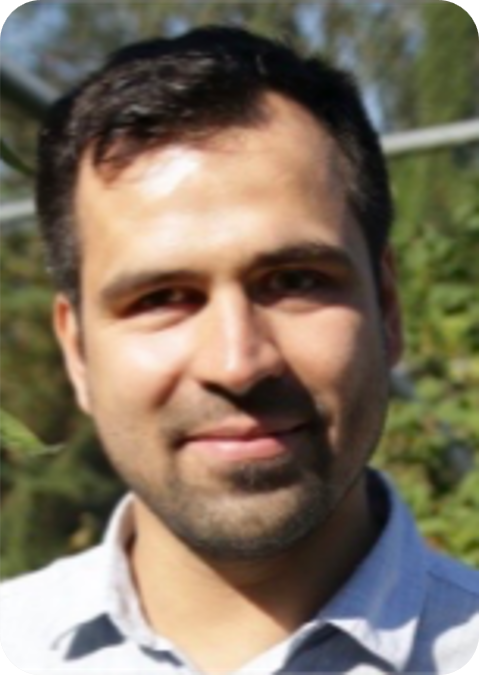 A man with short dark hair and a trimmed beard is smiling slightly outdoors, wearing a light-coloured collared shirt. Greenery, hinting at climate-resilient agriculture, is visible in the blurred background.