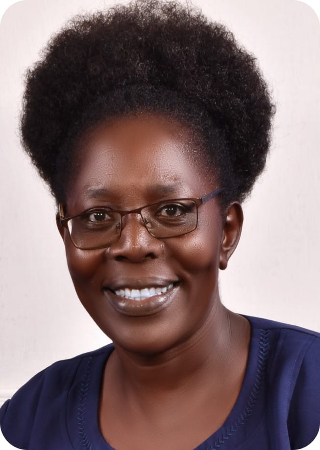 A woman with short curly hair, wearing glasses and a navy blue top, smiles at the camera against a plain light background, embodying her passion for ecophysiology and food security.