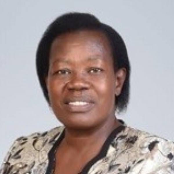 A woman with short black hair wearing a patterned beige and black top, posing in front of a plain light background, represents the dedication behind MultiStress Research focused on improving maize for global food security.
