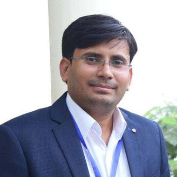 A man wearing glasses, a dark blue suit, and a white shirt stands in front of a light-coloured pillar, looking at the camera with a slight smile—a fitting image for discussions on maize crop modelling and food security.